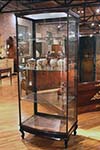 english glass and wood display cabinet with shelves , one large door, curved front.